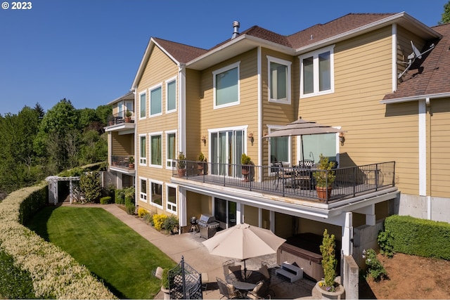 back of house with a lawn, a balcony, a patio area, and a hot tub