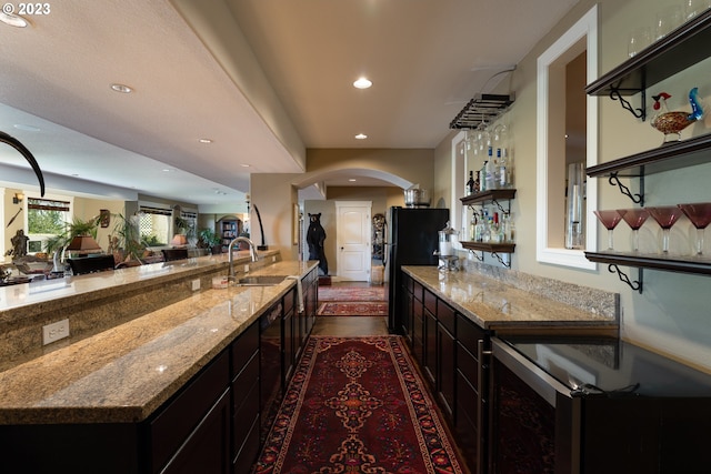 kitchen with dishwashing machine, dark brown cabinets, sink, and light stone countertops