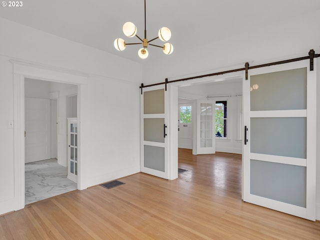 spare room with a barn door, an inviting chandelier, and light tile floors