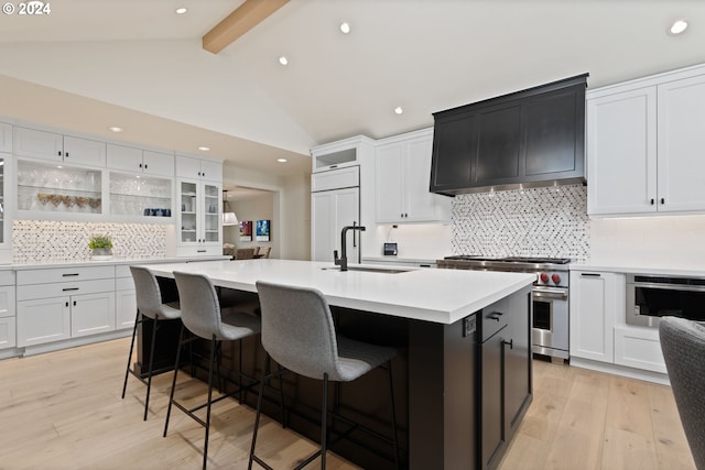 kitchen featuring light wood finished floors, beamed ceiling, high quality appliances, an island with sink, and light countertops