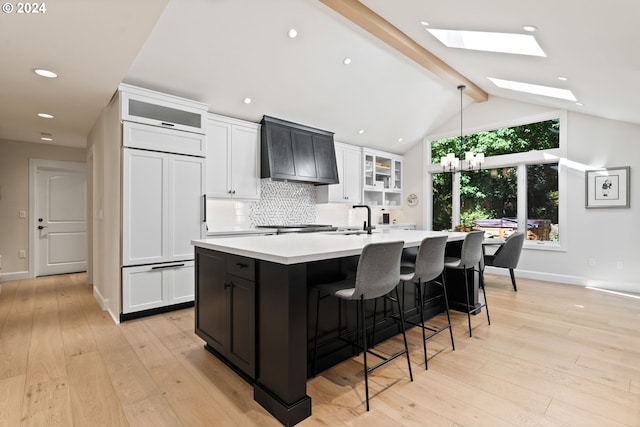 kitchen featuring premium range hood, paneled refrigerator, lofted ceiling with skylight, a kitchen island with sink, and decorative backsplash