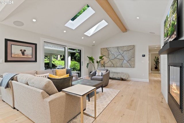 living area featuring beamed ceiling, a skylight, light wood-style floors, and a glass covered fireplace