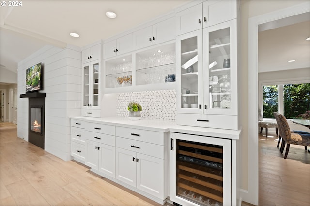 bar with wine cooler, a glass covered fireplace, light wood finished floors, and tasteful backsplash