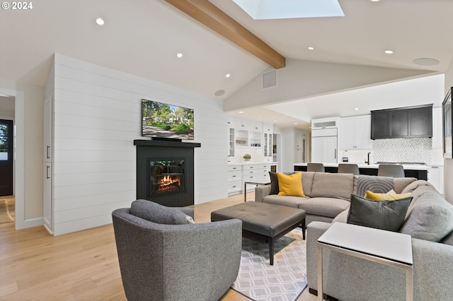 living area featuring a glass covered fireplace, beam ceiling, recessed lighting, and light wood-type flooring