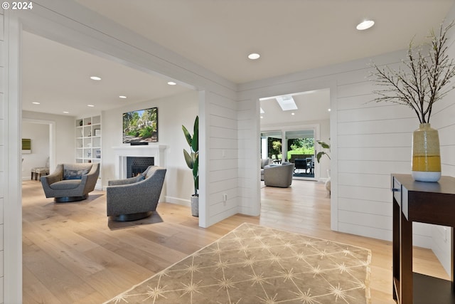 living room featuring light wood finished floors, wooden walls, built in shelves, a lit fireplace, and recessed lighting