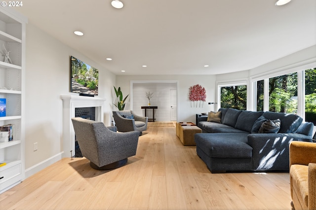 living area with light wood finished floors, built in shelves, baseboards, a tiled fireplace, and recessed lighting