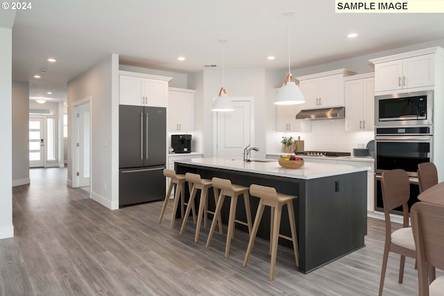 kitchen featuring white cabinetry, light hardwood / wood-style floors, pendant lighting, a center island with sink, and appliances with stainless steel finishes