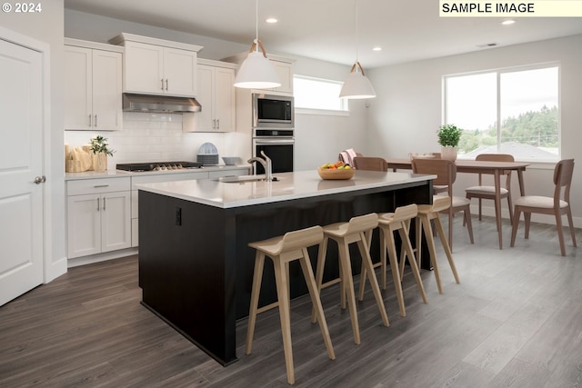 kitchen with pendant lighting, stainless steel appliances, white cabinetry, and a center island with sink