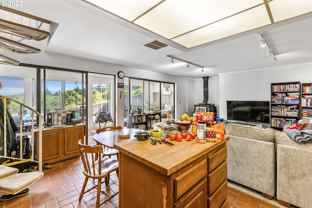 kitchen featuring a kitchen bar, rail lighting, a wood stove, a center island, and tile floors