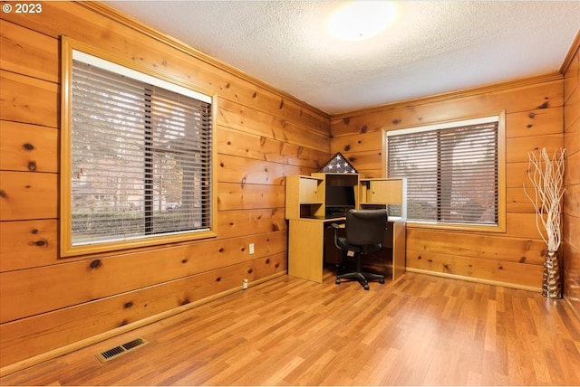 office area with a textured ceiling, light wood-type flooring, and wood walls