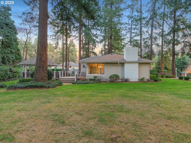 back house at dusk featuring a wooden deck and a lawn