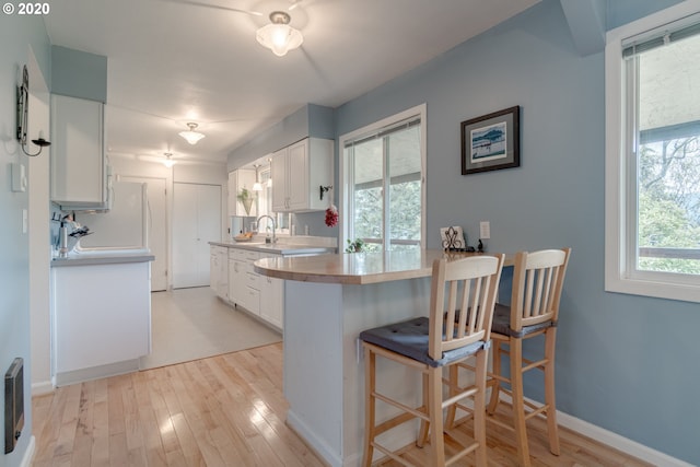 kitchen featuring light wood-type flooring, a kitchen bar, and white cabinetry