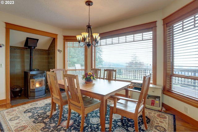 dining space featuring a wood stove, a wealth of natural light, lofted ceiling, and a notable chandelier