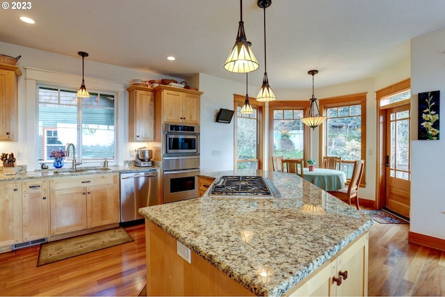 kitchen with pendant lighting, light wood-type flooring, sink, a kitchen island, and appliances with stainless steel finishes