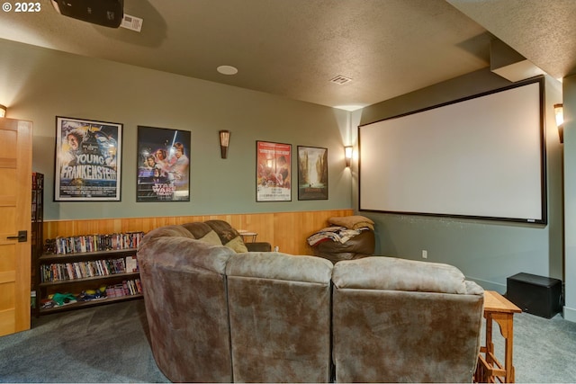 home theater room with a textured ceiling, wooden walls, and carpet flooring