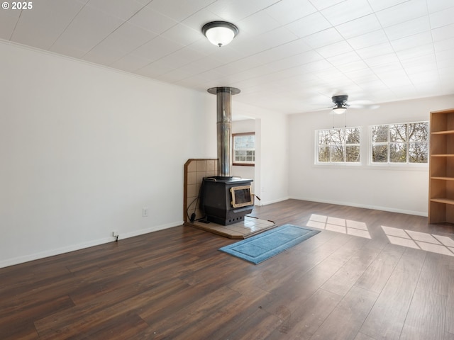 unfurnished living room with a wood stove, a ceiling fan, baseboards, and wood finished floors