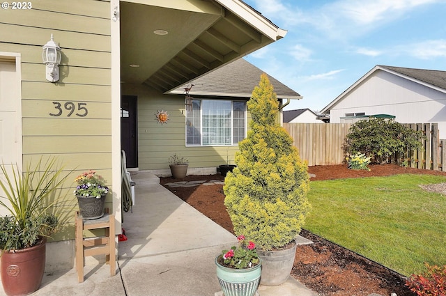 view of exterior entry featuring a yard, fence, and a shingled roof