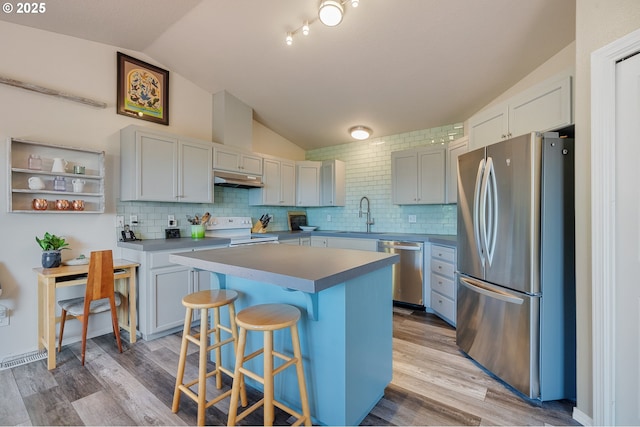 38225 Hiagua Ln N, Nehalem, OR 97131 - kitchen featuring stainless steel appliances, vaulted ceiling, a kitchen breakfast bar, under cabinet range hood, and tasteful backsplash