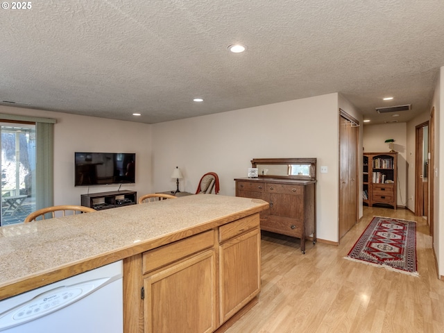 kitchen with light wood finished floors, dishwasher, a textured ceiling, and visible vents