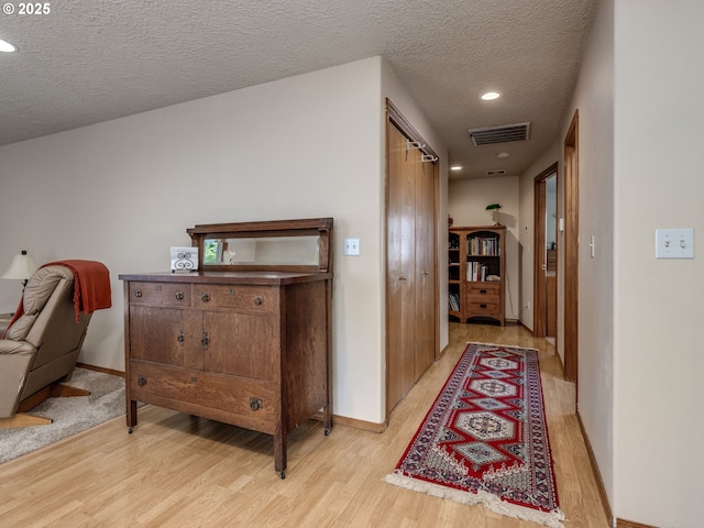 hallway featuring baseboards, light wood-style floors, visible vents, and a textured ceiling