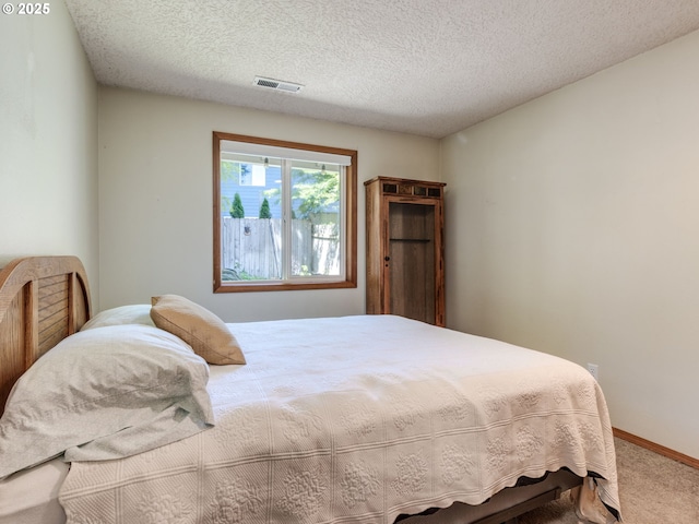 carpeted bedroom featuring a textured ceiling, baseboards, and visible vents