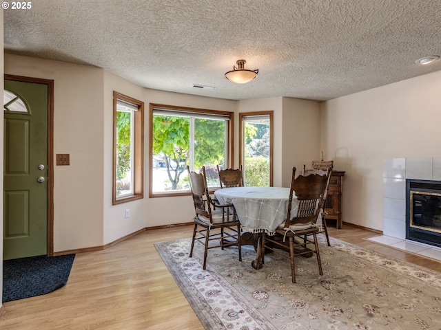 dining area featuring baseboards, a tile fireplace, light wood-style flooring, and a textured ceiling