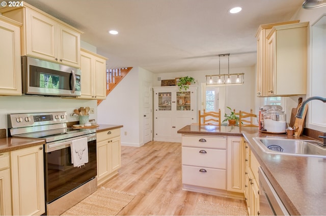 kitchen featuring stainless steel appliances, sink, decorative light fixtures, cream cabinetry, and light hardwood / wood-style floors