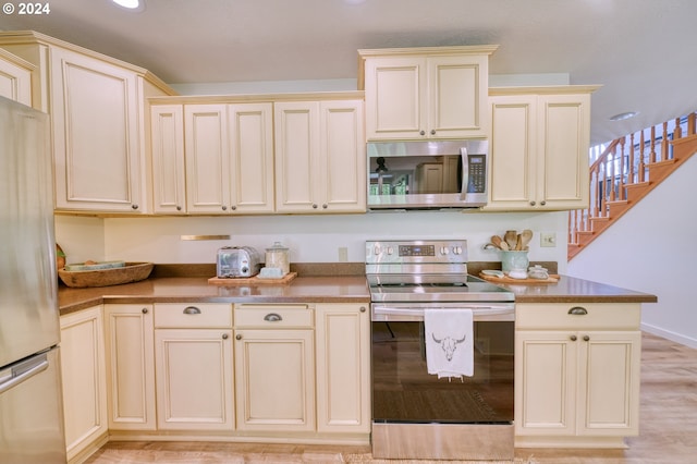 kitchen with cream cabinets, stainless steel appliances, and light hardwood / wood-style flooring