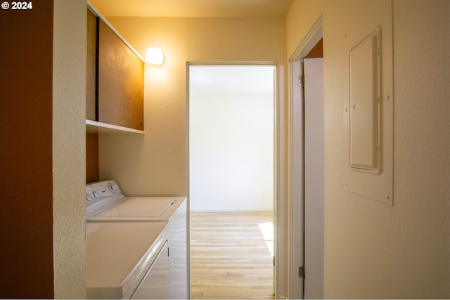 clothes washing area with washing machine and dryer, electric panel, and light hardwood / wood-style flooring