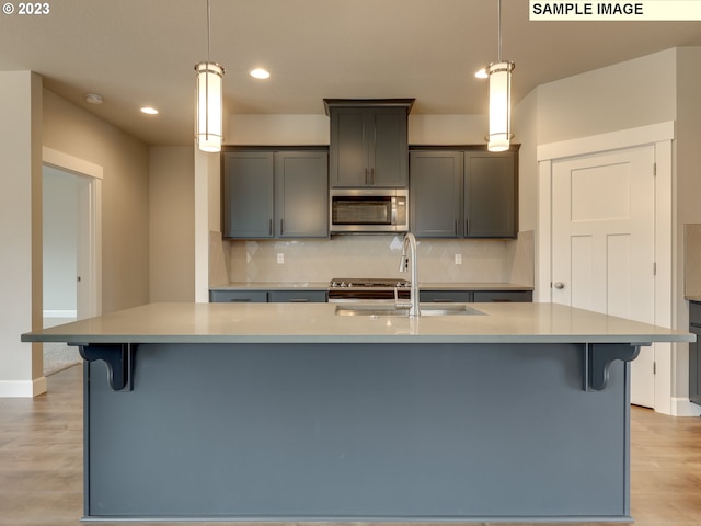 kitchen with decorative light fixtures, a kitchen island with sink, backsplash, and light hardwood / wood-style flooring