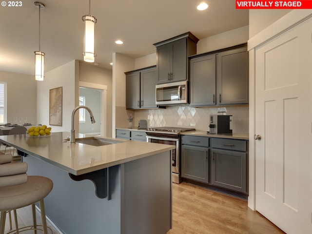 kitchen featuring decorative light fixtures, light hardwood / wood-style floors, stainless steel appliances, tasteful backsplash, and sink