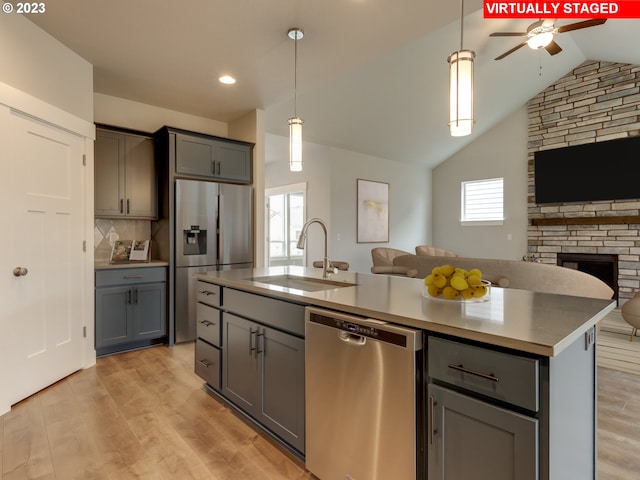 kitchen featuring light hardwood / wood-style floors, stainless steel appliances, a center island with sink, a fireplace, and backsplash