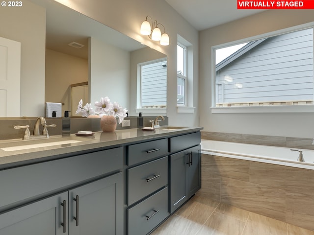 bathroom featuring tile flooring, tiled tub, and double sink vanity