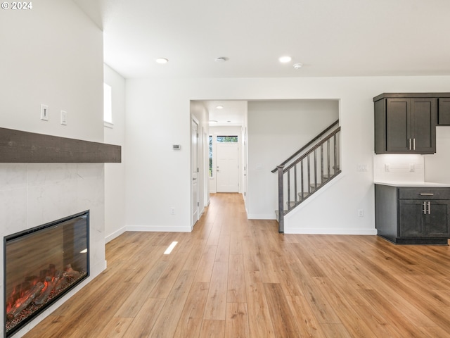 unfurnished living room with a tiled fireplace, a healthy amount of sunlight, and light wood-type flooring