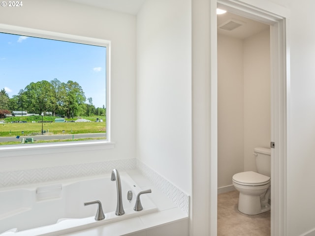 bathroom featuring a healthy amount of sunlight, tiled bath, and toilet