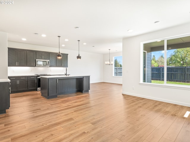 kitchen with a chandelier, a center island with sink, appliances with stainless steel finishes, light hardwood / wood-style floors, and pendant lighting