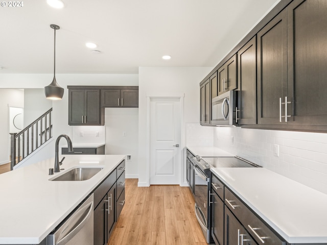 kitchen with sink, light hardwood / wood-style flooring, a center island with sink, pendant lighting, and appliances with stainless steel finishes