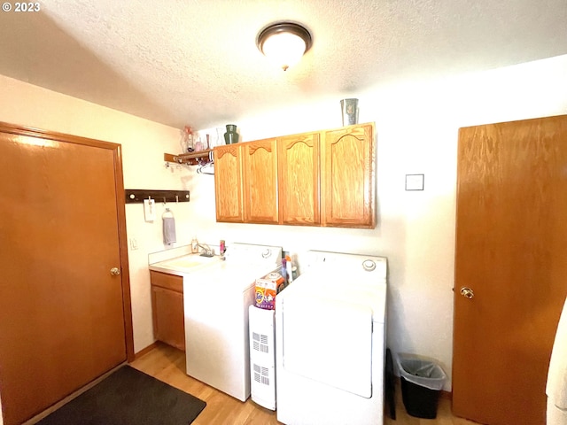 laundry room with light hardwood / wood-style flooring, washer / dryer, a textured ceiling, and cabinets