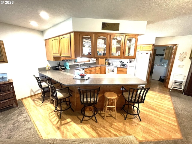 kitchen with a breakfast bar, washer / clothes dryer, a textured ceiling, kitchen peninsula, and light hardwood / wood-style flooring