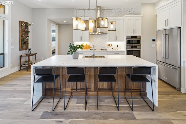 kitchen with a center island with sink, appliances with stainless steel finishes, light hardwood / wood-style floors, and pendant lighting