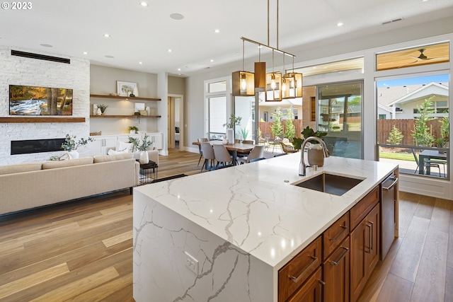 kitchen featuring pendant lighting, an island with sink, a fireplace, light hardwood / wood-style floors, and sink