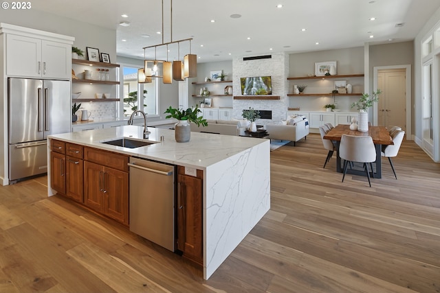 kitchen with stainless steel appliances, light wood-type flooring, a stone fireplace, and sink