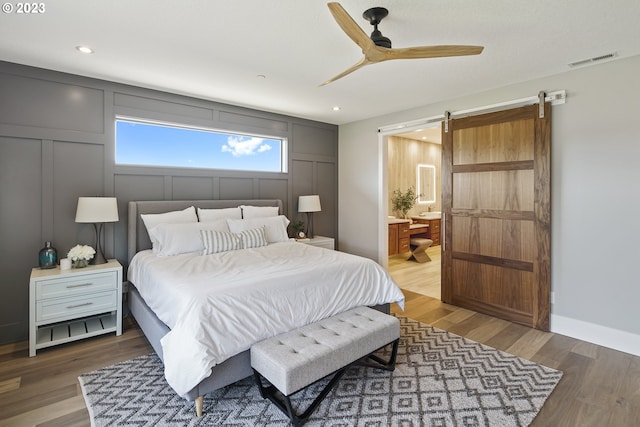 bedroom with a barn door, ensuite bathroom, ceiling fan, and dark wood-type flooring