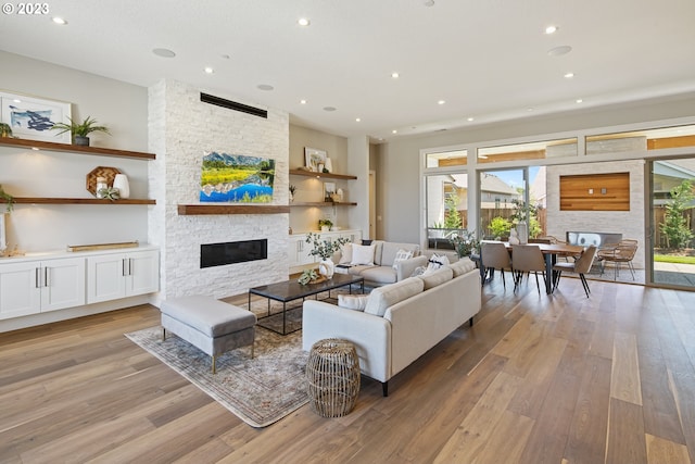 living room with light hardwood / wood-style flooring, a stone fireplace, and a healthy amount of sunlight