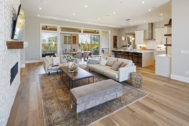 living room featuring a notable chandelier, sink, light wood-type flooring, and a stone fireplace