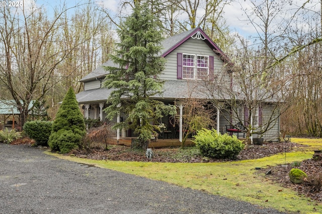 view of front of house with covered porch, roof with shingles, and a front yard