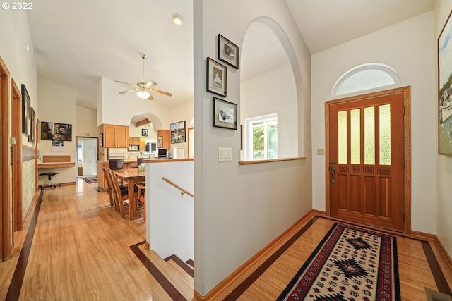 foyer with high vaulted ceiling, ceiling fan, and light wood-type flooring