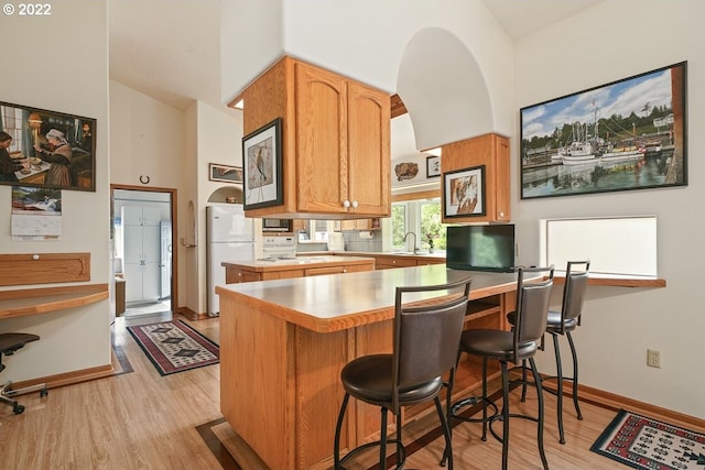 kitchen with a kitchen breakfast bar, white refrigerator, kitchen peninsula, high vaulted ceiling, and light hardwood / wood-style flooring