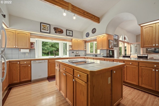 kitchen with backsplash, tile counters, white dishwasher, vaulted ceiling with beams, and light hardwood / wood-style flooring