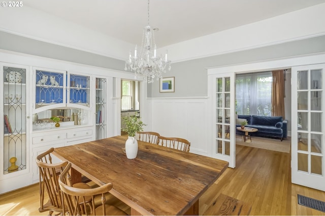 2147 NE 14th Ave, Portland, OR 97212 - dining space featuring a chandelier, light wood finished floors, a wainscoted wall, french doors, and a decorative wall